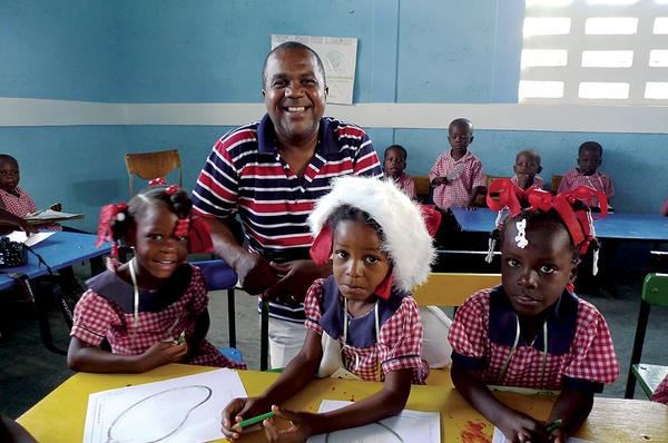 Tony Boursiquot stands with children at a Star of Hope school in Jeanton, Haiti, 60 miles north of Port-au-Prince. He was born in a village in southern Haiti, then went to live with relatives in the capital. He worked for an American woman who paid for his college in exchange for being her driver and houseboy.  <P>Gary G. Yerkey