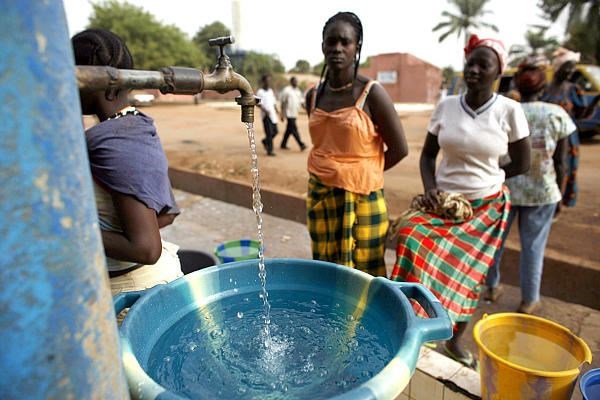 Girls fill plastic basins at a free water tap operated by a charity in a neighborhood of Bissau, Gui