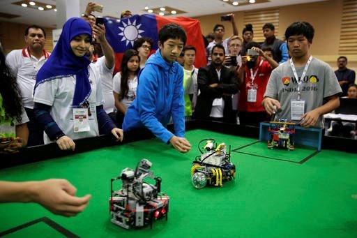 In this Sunday, Nov. 27, 2016, photo, participants from Taiwan watch their robots playing a soccer match during the World Robot Olympiad in New Delhi, India. The weekend games brought more than 450 teams of students from 50 countries to the Indian capital. (AP Photo/Tsering Topgyal)