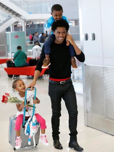 Olympic silver medalist Feyisa Lilesa, of Ethiopia, carries his son Sora, 3, and pulls along his daughter Soko, 5, after picking up his family at Miami International Airport, Tuesday, Feb. 14, 2017, in Miami. Lilesa arrived in the U.S. on a special skills visa, which allows him to train and compete until January. His wife, son, daughter and brother joined him in Miami Tuesday. (AP Photo/Wilfredo Lee)