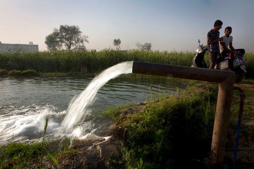 Indians sit on a two-wheeler and talk as water from a bore well irrigates their field on the World Water Day on the outskirts of New Delhi, India, Wednesday, March 22, 2017. India has the world's highest number of people without access to clean water. UNICEF says nearly 78 million Indians - about 5 percent of the country's 1.3 billion population - must make do with contaminated water sources or buy water at high rates. (AP Photo/Manish Swarup)