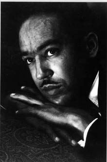 Black and white photo of Langston Hughes looking upward, resting his head on his hand.